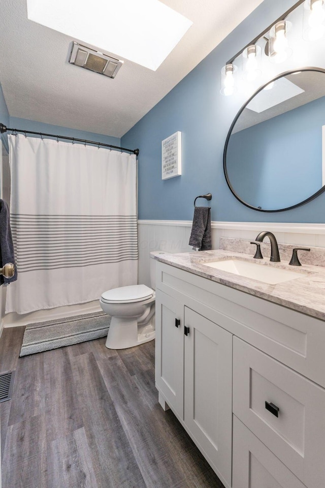 bathroom with visible vents, toilet, a wainscoted wall, wood finished floors, and vanity