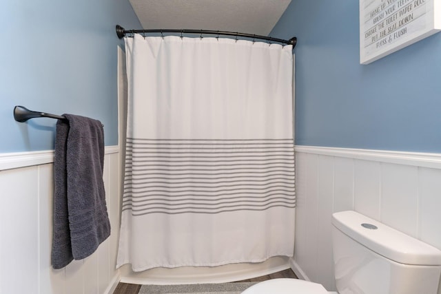 bathroom featuring a textured ceiling, wainscoting, toilet, and shower / tub combo with curtain