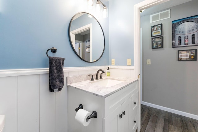 bathroom with a wainscoted wall, wood finished floors, vanity, and visible vents