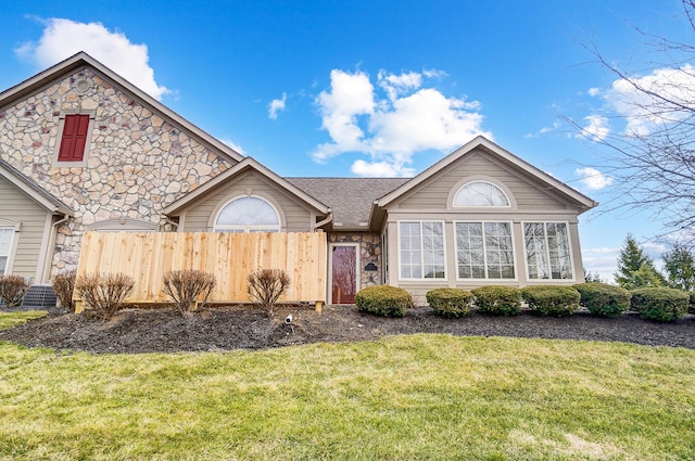 ranch-style home featuring a front lawn, fence, and stone siding