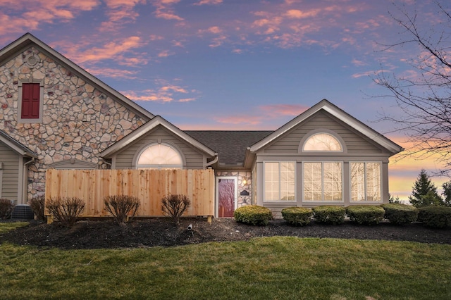 single story home with stone siding, a shingled roof, a front lawn, and fence