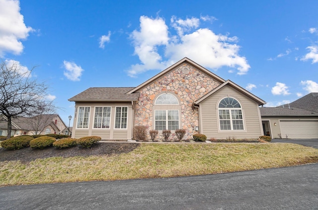 ranch-style home featuring a front lawn, driveway, a garage, and stone siding