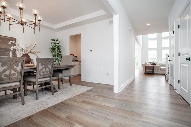 dining space featuring an inviting chandelier, light wood-type flooring, and a tray ceiling