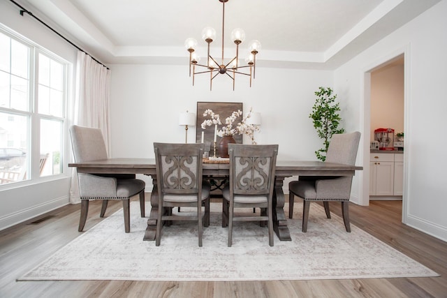 dining room with an inviting chandelier, a tray ceiling, and light wood-type flooring