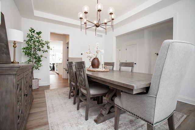 dining area with an inviting chandelier, a raised ceiling, and light hardwood / wood-style flooring