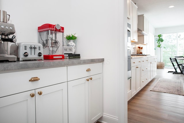 kitchen featuring stainless steel gas cooktop, wall chimney range hood, light hardwood / wood-style floors, and white cabinets