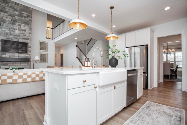 kitchen with pendant lighting, appliances with stainless steel finishes, a kitchen island with sink, and white cabinets