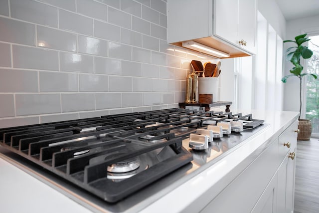 room details featuring backsplash, stainless steel gas cooktop, and white cabinets