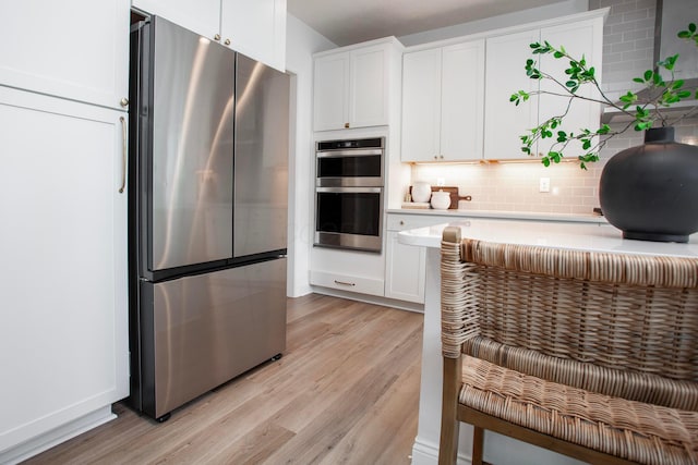 kitchen with tasteful backsplash, stainless steel appliances, light hardwood / wood-style floors, and white cabinets