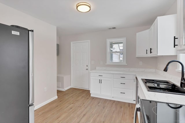 kitchen with sink, stainless steel fridge, white cabinetry, light stone countertops, and light wood-type flooring