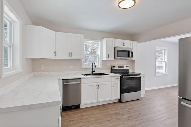 kitchen featuring sink, white cabinetry, light stone counters, light wood-type flooring, and stainless steel appliances