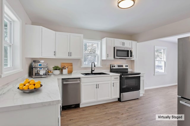 kitchen with sink, white cabinets, light stone counters, light hardwood / wood-style floors, and stainless steel appliances