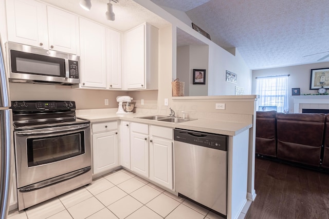 kitchen featuring sink, appliances with stainless steel finishes, a textured ceiling, white cabinets, and kitchen peninsula