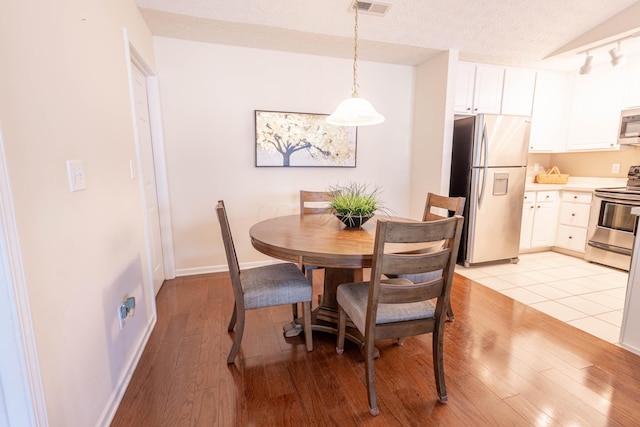 dining area featuring vaulted ceiling, a textured ceiling, and light wood-type flooring