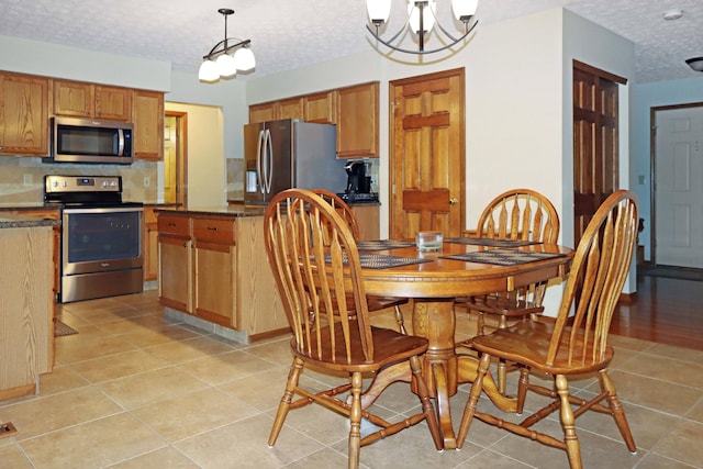 kitchen with light tile patterned floors, appliances with stainless steel finishes, a notable chandelier, a textured ceiling, and decorative light fixtures