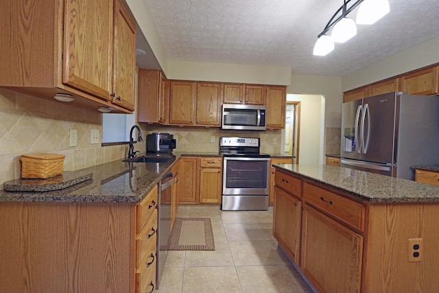 kitchen with sink, light tile patterned floors, dark stone countertops, appliances with stainless steel finishes, and a kitchen island