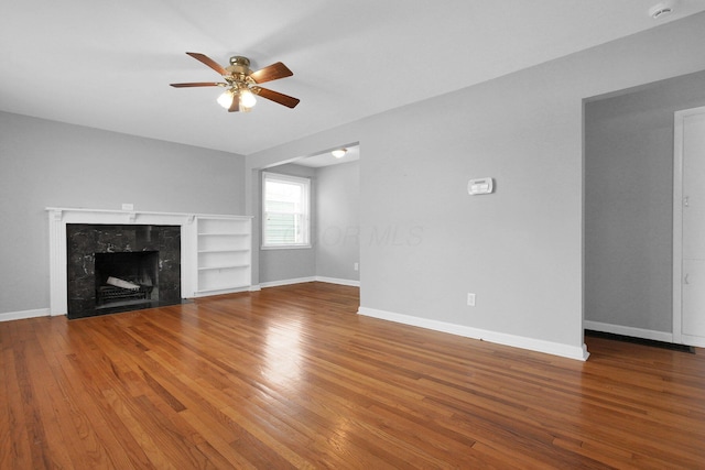 unfurnished living room featuring hardwood / wood-style floors, a high end fireplace, built in features, and ceiling fan