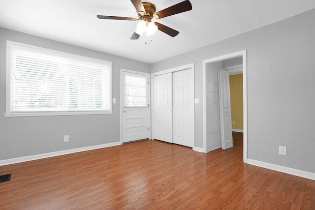 unfurnished bedroom with ceiling fan, hardwood / wood-style floors, a closet, and multiple windows