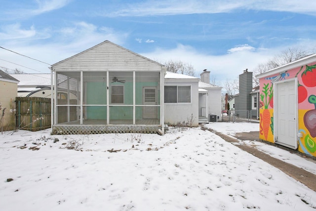 snow covered back of property with a sunroom and ceiling fan