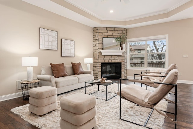 living room featuring a large fireplace, dark hardwood / wood-style flooring, ornamental molding, ceiling fan, and a raised ceiling