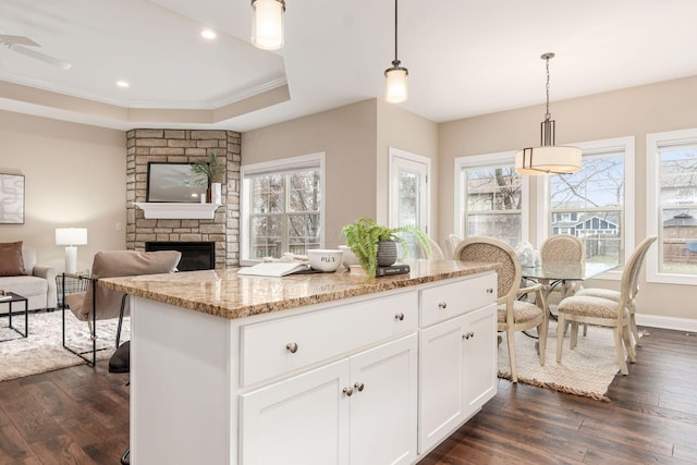 kitchen with dark wood-type flooring, white cabinetry, light stone counters, hanging light fixtures, and a tray ceiling