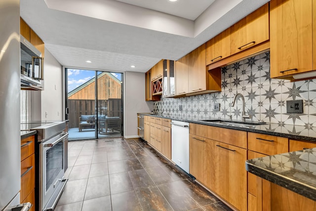 kitchen with tasteful backsplash, appliances with stainless steel finishes, sink, and dark stone countertops