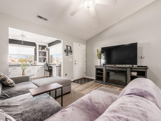 living room with ceiling fan, lofted ceiling, built in desk, and light wood-type flooring