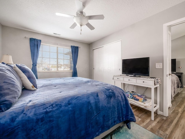 bedroom featuring wood-type flooring, a textured ceiling, ceiling fan, and a closet