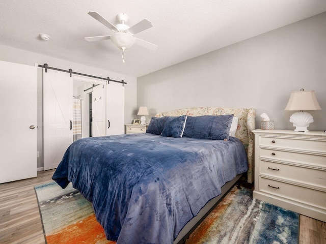 bedroom with a barn door, hardwood / wood-style floors, a textured ceiling, and ceiling fan