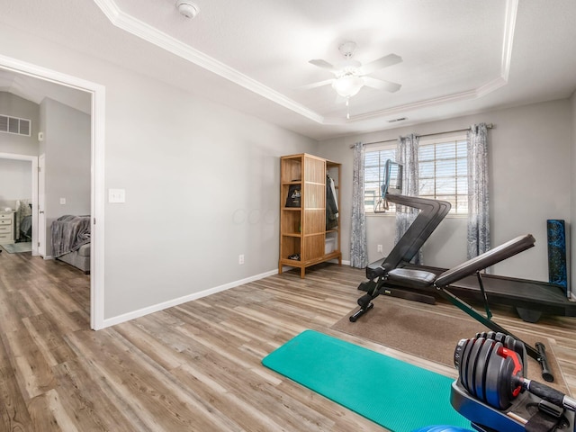 workout area featuring hardwood / wood-style flooring, ceiling fan, ornamental molding, and a tray ceiling