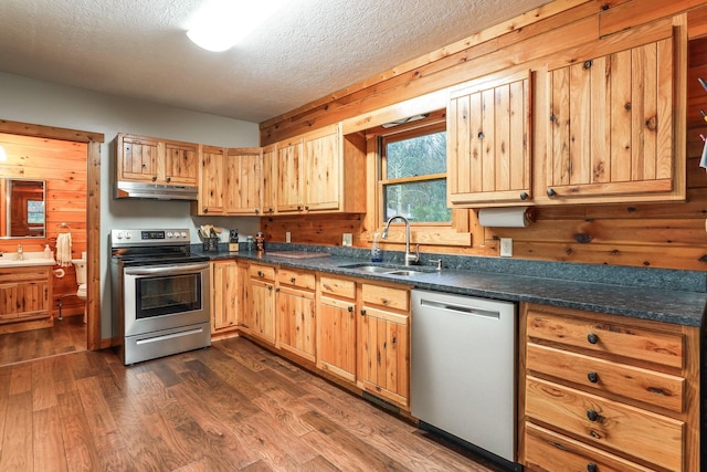 kitchen with appliances with stainless steel finishes, wood walls, sink, dark wood-type flooring, and a textured ceiling