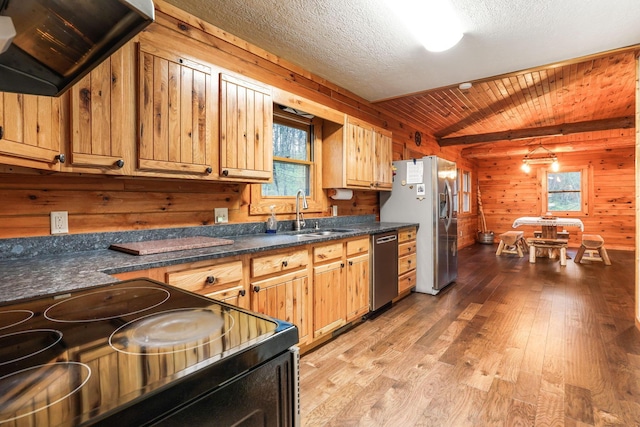 kitchen featuring wooden walls, sink, stainless steel appliances, a textured ceiling, and light hardwood / wood-style flooring