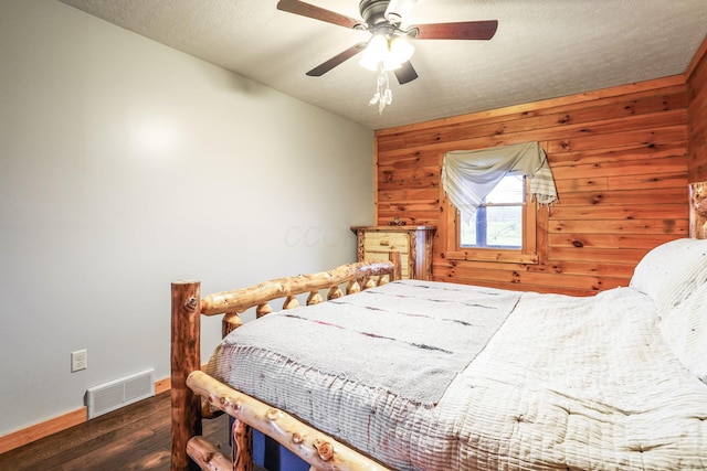 bedroom featuring ceiling fan, wooden walls, dark hardwood / wood-style floors, and a textured ceiling