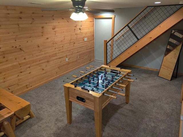 recreation room featuring dark colored carpet, ceiling fan, and wooden walls