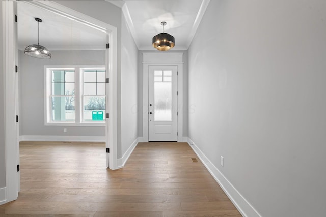 foyer featuring light wood finished floors, ornamental molding, plenty of natural light, and baseboards