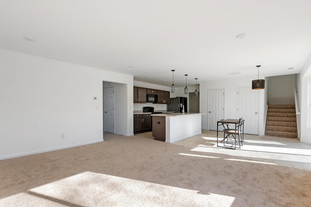 kitchen with pendant lighting, black appliances, a center island with sink, dark brown cabinets, and light carpet