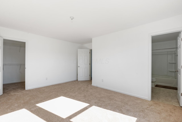 unfurnished bedroom featuring ensuite bathroom, a walk in closet, light carpet, and a closet