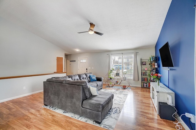 living room with ceiling fan, vaulted ceiling, a textured ceiling, and light hardwood / wood-style floors