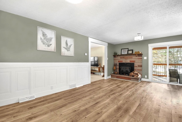 unfurnished living room with wood-type flooring, a textured ceiling, and a wood stove