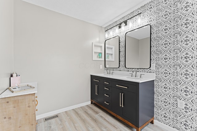 bathroom with baseboards, wood finished floors, a sink, and wallpapered walls