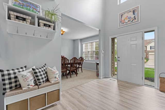 foyer featuring light wood finished floors, baseboards, and a towering ceiling
