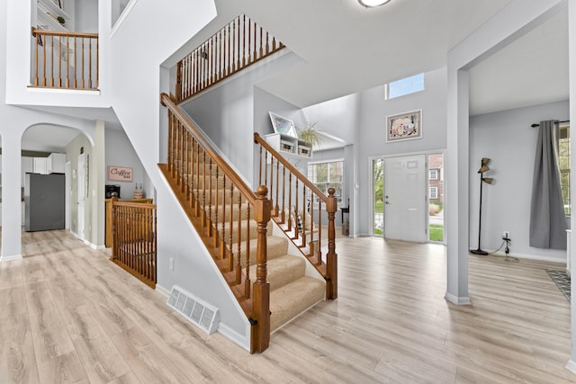 staircase featuring wood finished floors, a towering ceiling, visible vents, and plenty of natural light