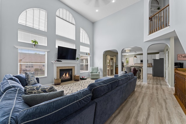 living area featuring arched walkways, light wood-style floors, a healthy amount of sunlight, and a towering ceiling
