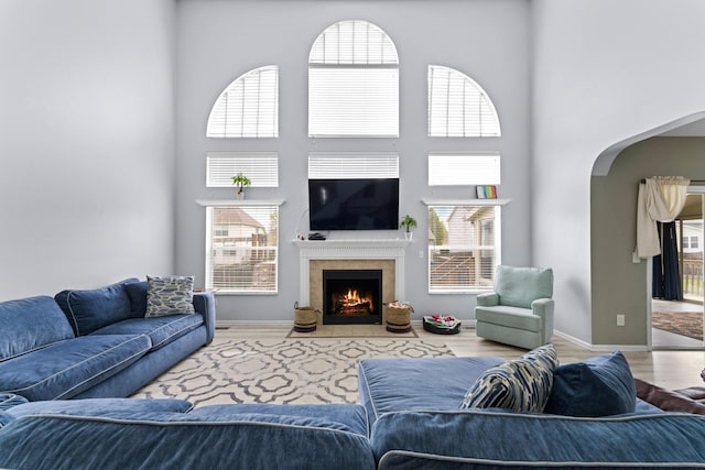 living area with a fireplace, wood finished floors, a wealth of natural light, and a towering ceiling