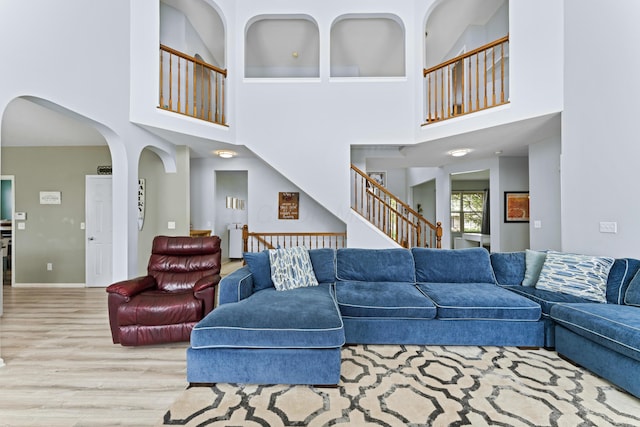 living area with a high ceiling, wood finished floors, arched walkways, baseboards, and stairs