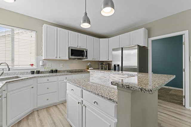 kitchen with stainless steel appliances, a sink, light wood-style floors, a kitchen island, and white cabinetry