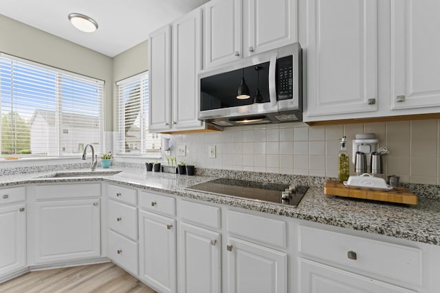 kitchen with a sink, white cabinets, decorative backsplash, black electric stovetop, and stainless steel microwave