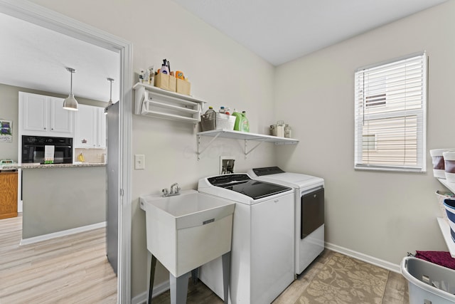 clothes washing area with washer and dryer, baseboards, light wood-style floors, and laundry area