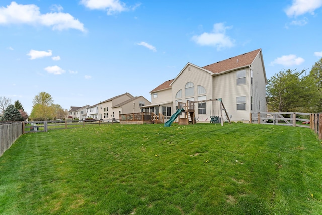 rear view of house with a fenced backyard, a deck, a yard, and a playground