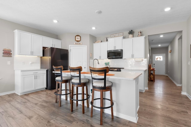 kitchen with a kitchen island with sink, a kitchen breakfast bar, white cabinets, and black fridge